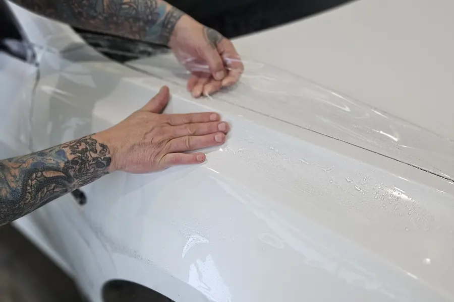 Installer smoothing paint protection film onto the fender of a white car