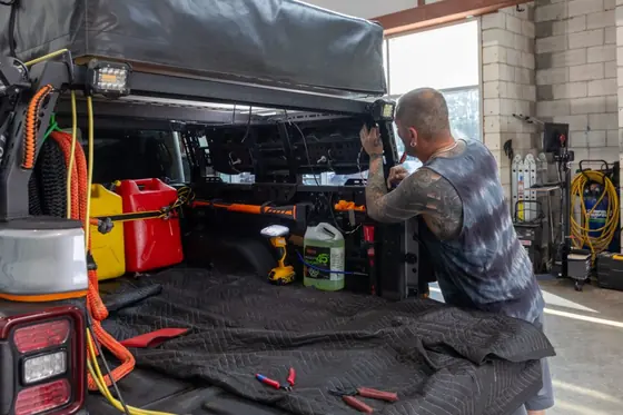 Installer fitting accessories inside a pickup truck bed in the shop